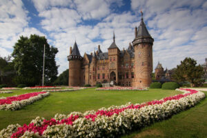 Foto van Kasteel de Haar, met een grasveld met bloemen op de voorgrond en een blauwe lucht met witte wolken boven het kasteel. Bron: https://www.ontdek-utrecht.nl/locatie/kasteel-de-haar